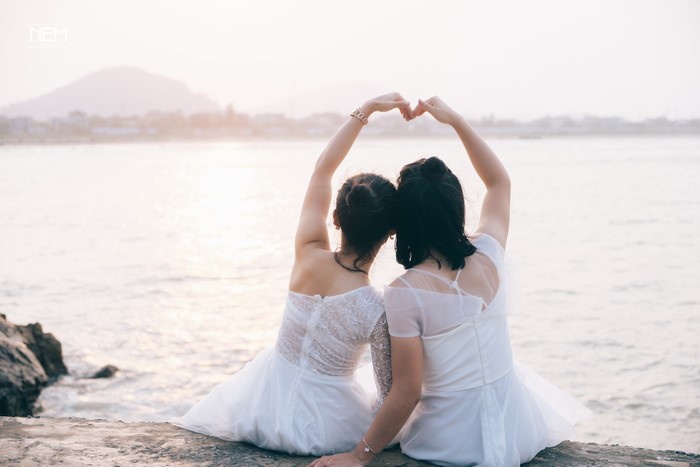 Two women in white dresses making heart shape