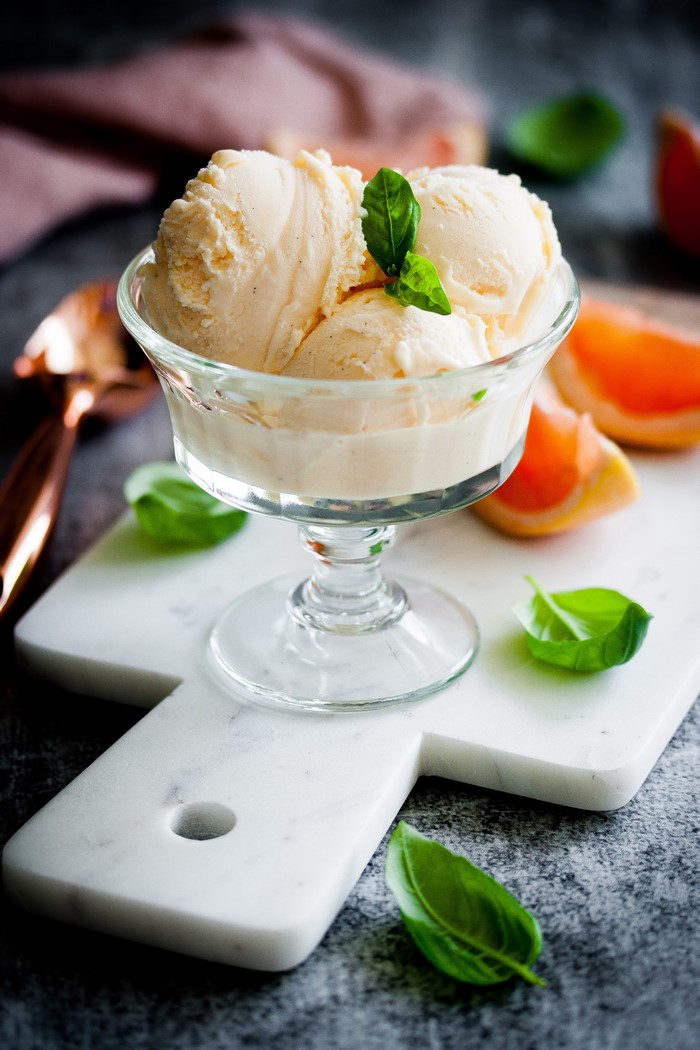 Vanilla ice cream scoops in a glass bowl with basil and grapefruit