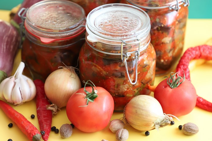 Jars of preserved vegetables with fresh produce
