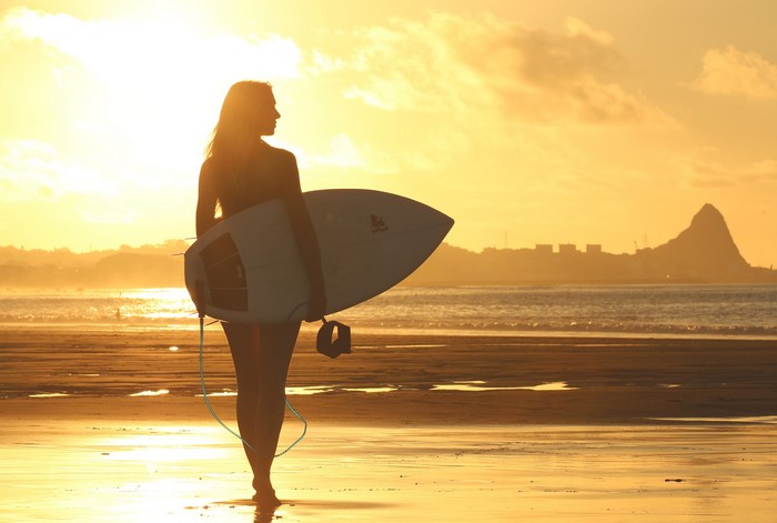 Surfer with surfboard on beach at sunset