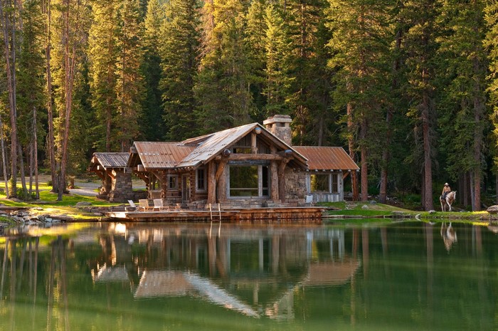 Log cabin by a lake in a forest with a person on horseback