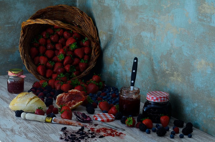 Still-life of strawberries, berries, jam, and bread in a basket