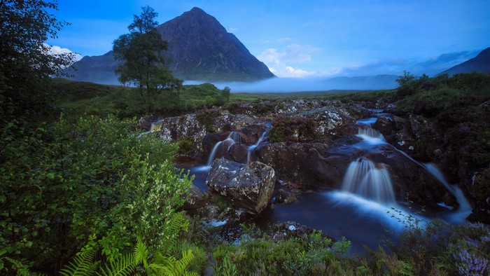 Waterfall flowing over rocks in Scotland with a mountain in the background