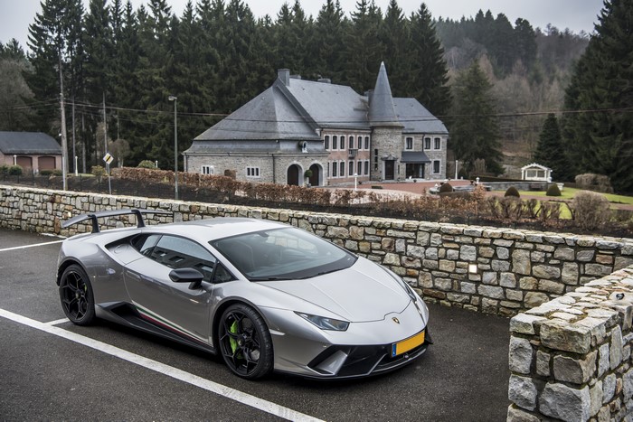 Grey Lamborghini Performante Huracan parked near a stone wall and mansion
