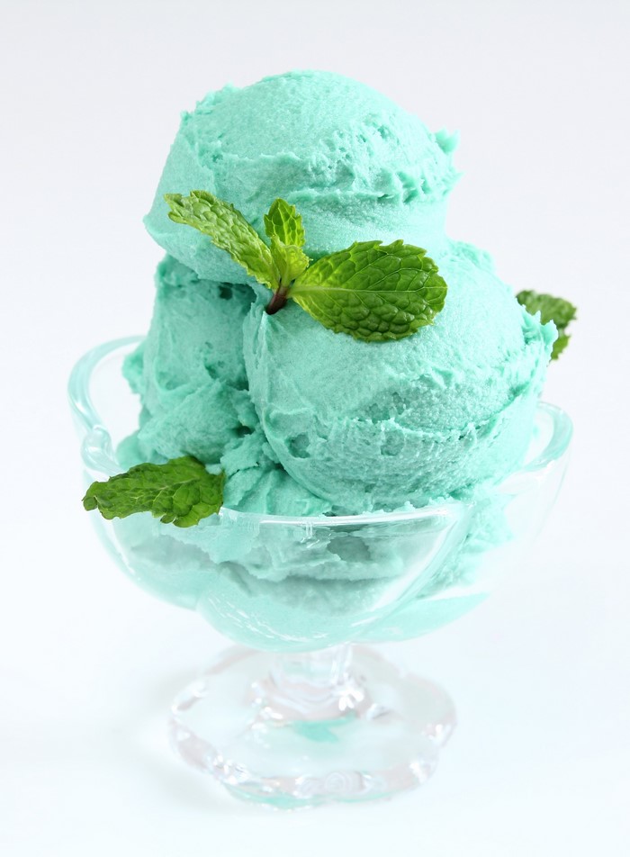 Mint ice cream scoops in a glass bowl with mint leaves