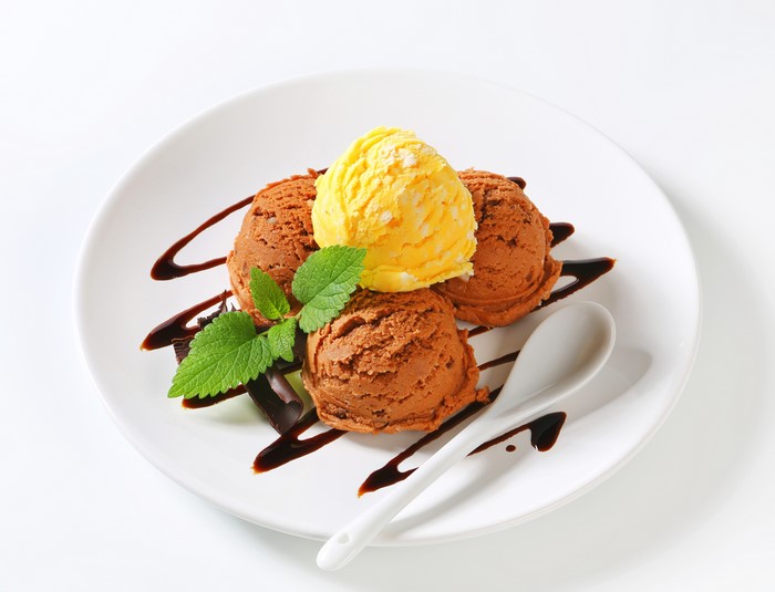Chocolate and yellow ice cream scoops on a plate with chocolate sauce