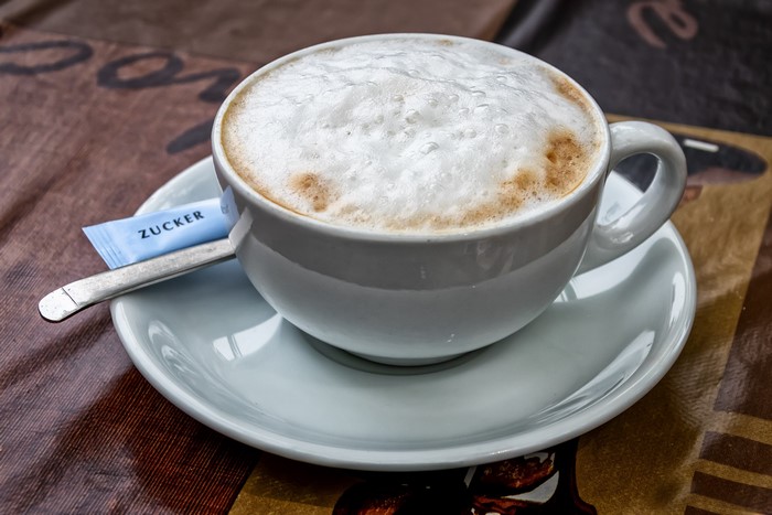Cappuccino in a white cup with sugar packet and spoon