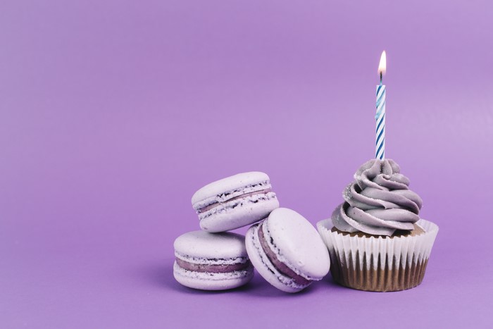 Cupcake with candle and macarons on purple background