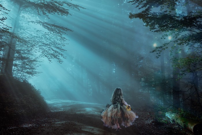 Little girl in a foggy forest with sun rays