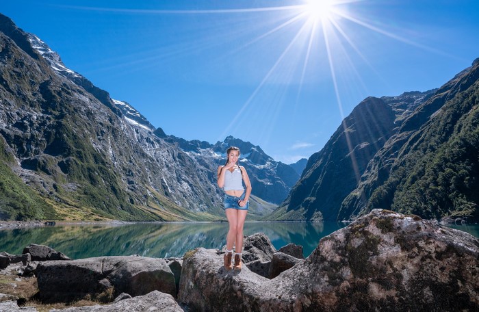 Woman posing by a mountain lake with sun rays