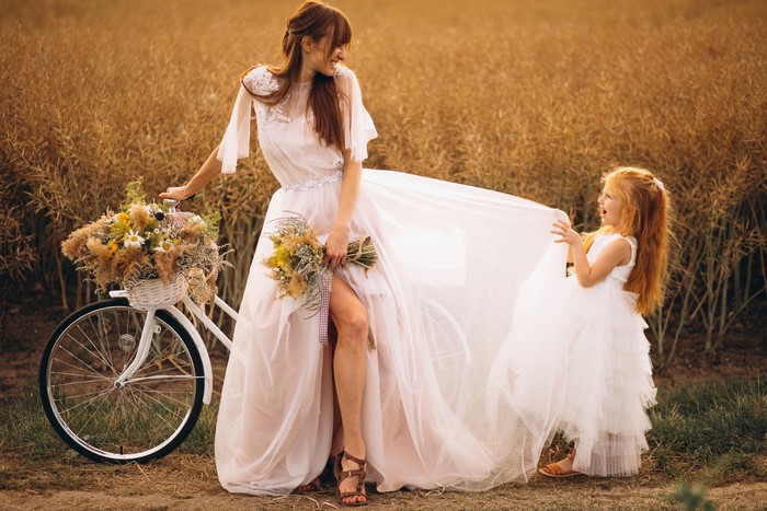 Bride and flower girl with bicycle in field