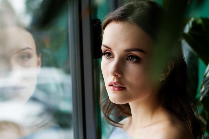 Brunette girl looking out a window with reflection