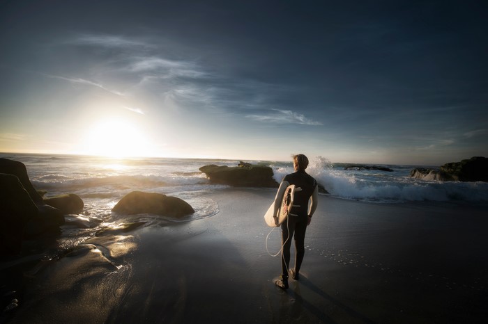 Surfer with surfboard on beach at sunset
