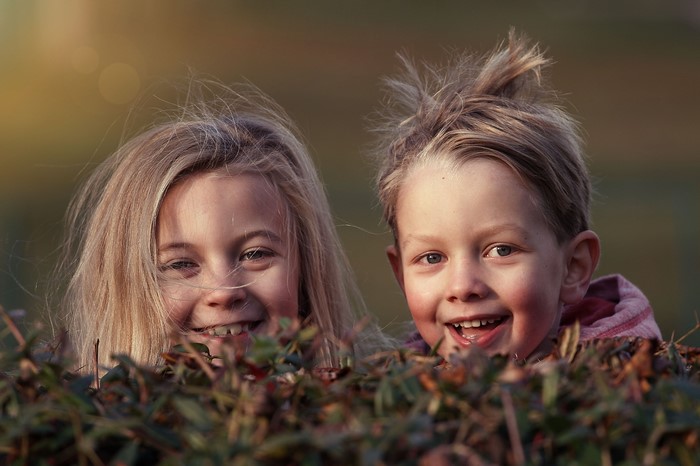 Two children peeking over a bush