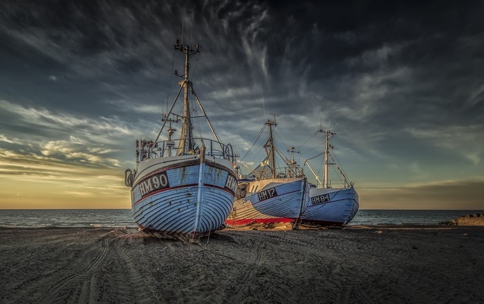 Three fishing boats on a sandy beach at sunset
