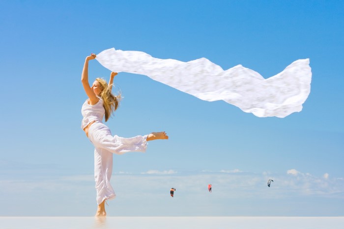 Woman in white holding a white scarf in the wind