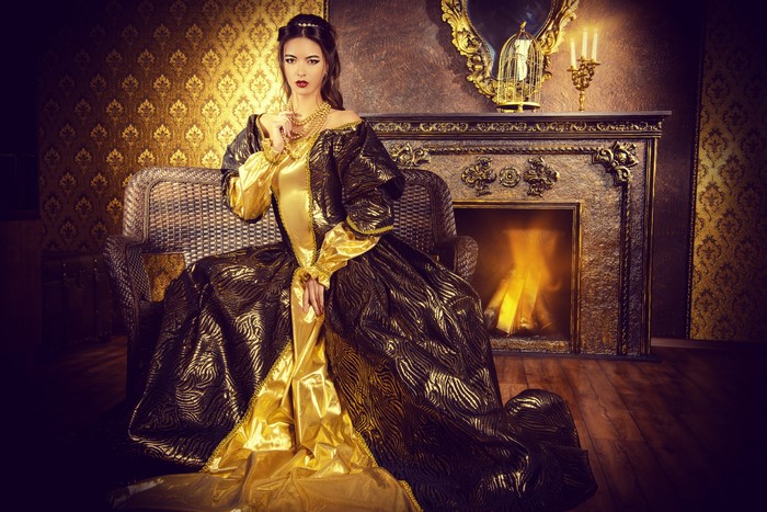 Woman in a vintage dress sitting by a fireplace
