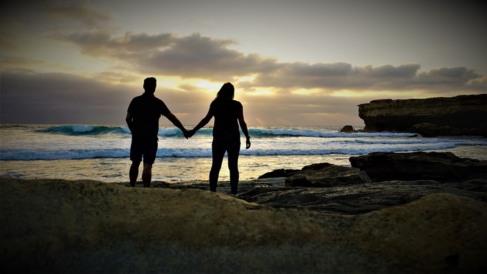 Couple holding hands on a rocky coast at sunset