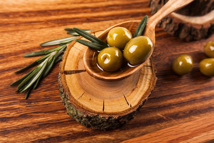 Olives in a wooden spoon with rosemary