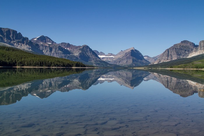 Mountains reflected in a clear lake under a blue sky