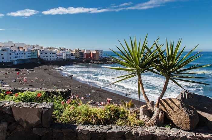 Black sand beach with colorful buildings and palm trees in Puerto de La Cruz, Tenerife