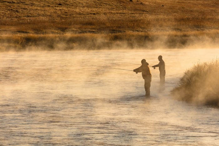 Two men fly fishing in a misty river at sunrise