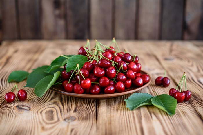 Cherries on a plate with leaves on wooden background