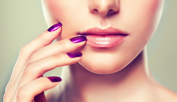 Close-up of woman's lips and hand with purple nails