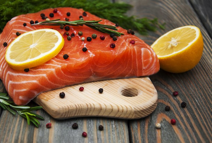 Raw salmon fillet with lemon and peppercorns on a cutting board