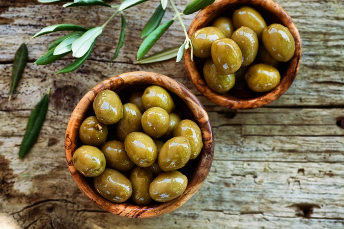 Green olives in wooden bowls with olive branches