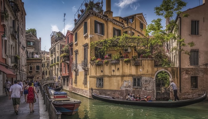 Venice canal with gondola and people walking along the street