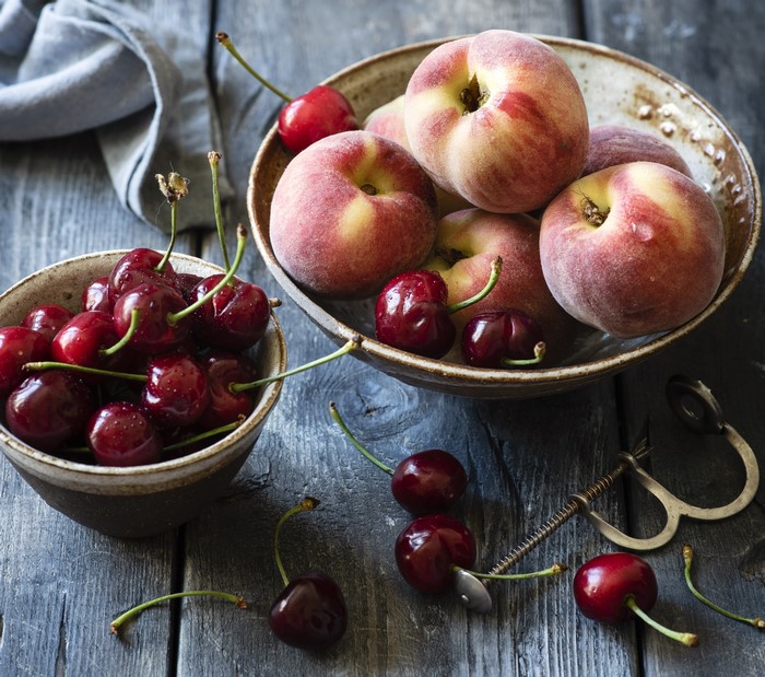 Peaches and cherries in bowls on wooden table