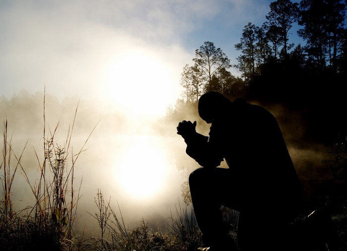 Man praying at sunrise by foggy lake