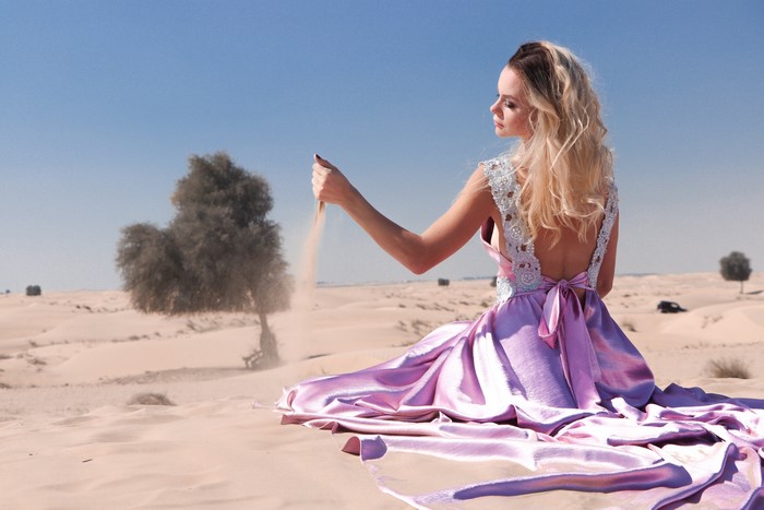 Woman in a dress in the desert letting sand fall from her hands