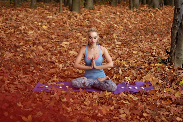 Woman meditating in lotus position in autumn forest