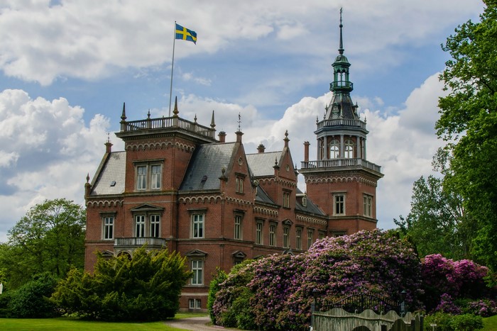 Kulla Gunnarstorp Castle with Swedish flag and flowering shrubs