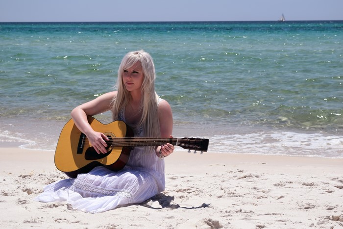 Blonde girl playing guitar on a beach