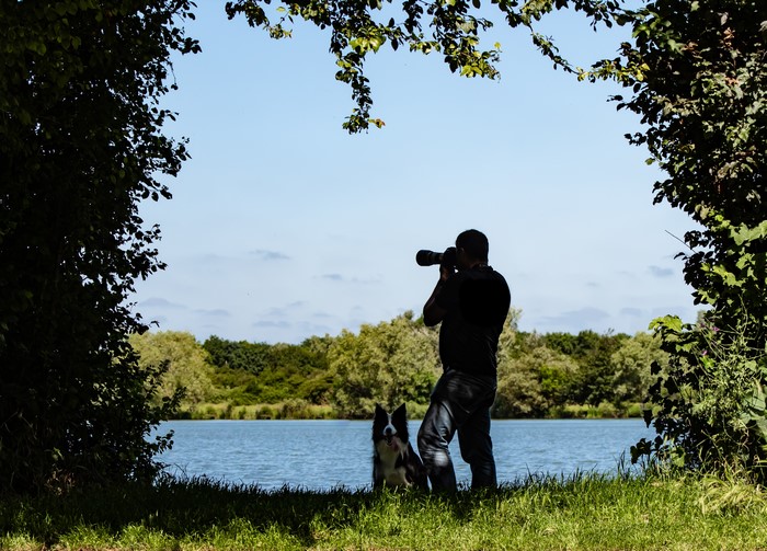 Man with dog photographing a lake