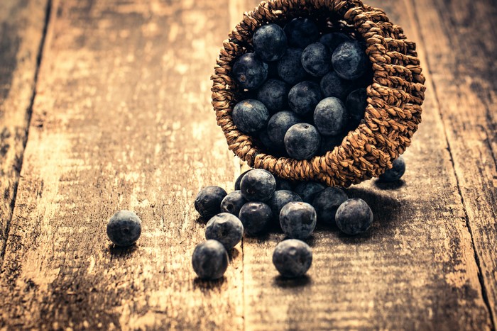 Blueberries spilling from a wicker basket on wood planks