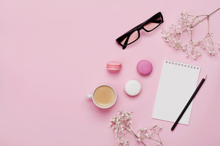 Coffee, macarons, glasses, notebook, and pencil on pink background