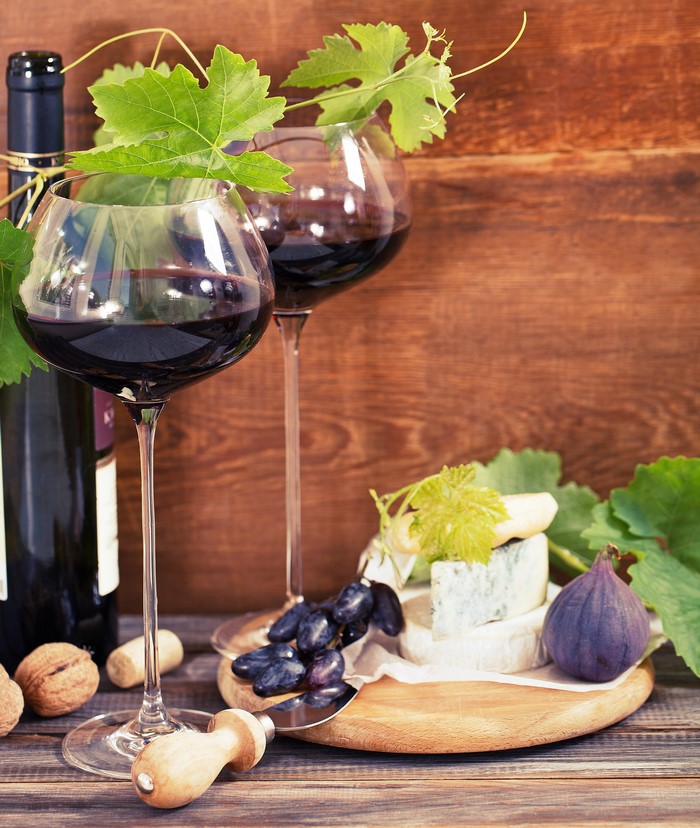 Wine bottle, glasses of red wine, cheese, grapes, fig, and nuts