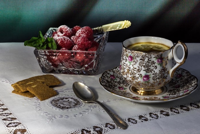 Raspberries in a crystal bowl with tea and cookies