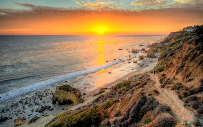 Sunset over a rocky beach with a cliffside path