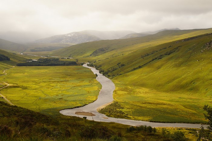 River flowing through green Scottish valley with fog