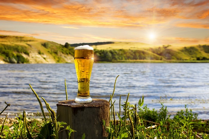 Beer in a highball glass on a tree stump by a river at sunset