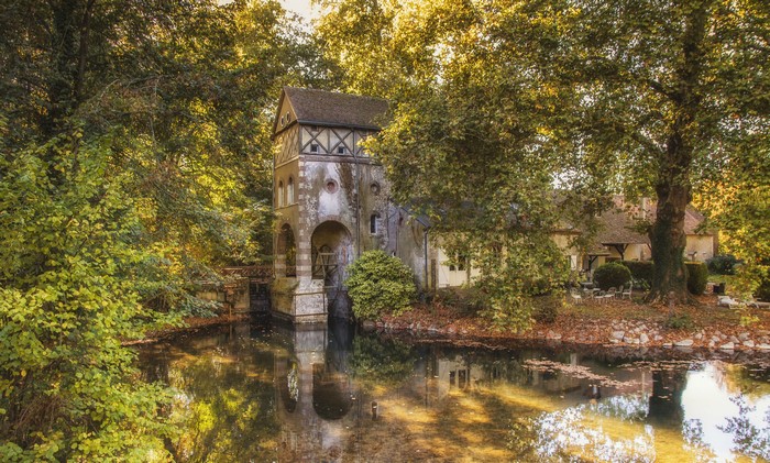 Old mill building by a pond surrounded by trees in France