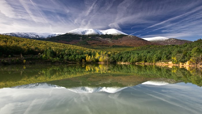 Snow-capped mountains reflected in a lake with autumn forests
