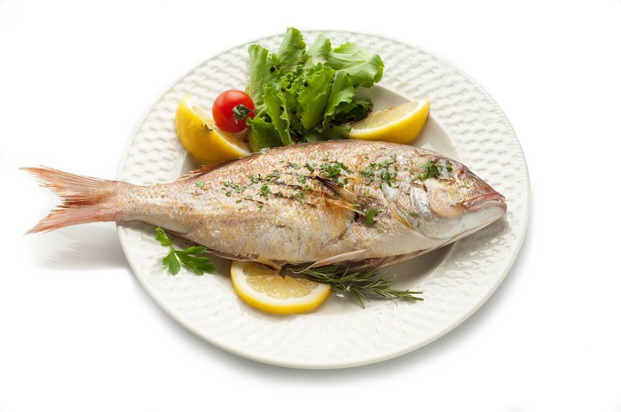 Whole cooked fish with lemon and lettuce on a plate
