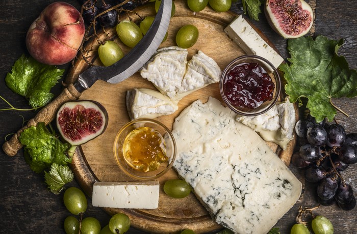 Cheese, Grapes, Figs, Peaches, and Jam on a Cutting Board