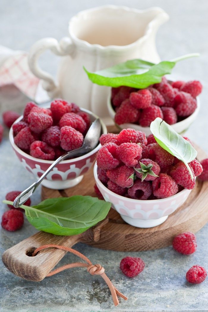 Raspberries in bowls with basil leaves